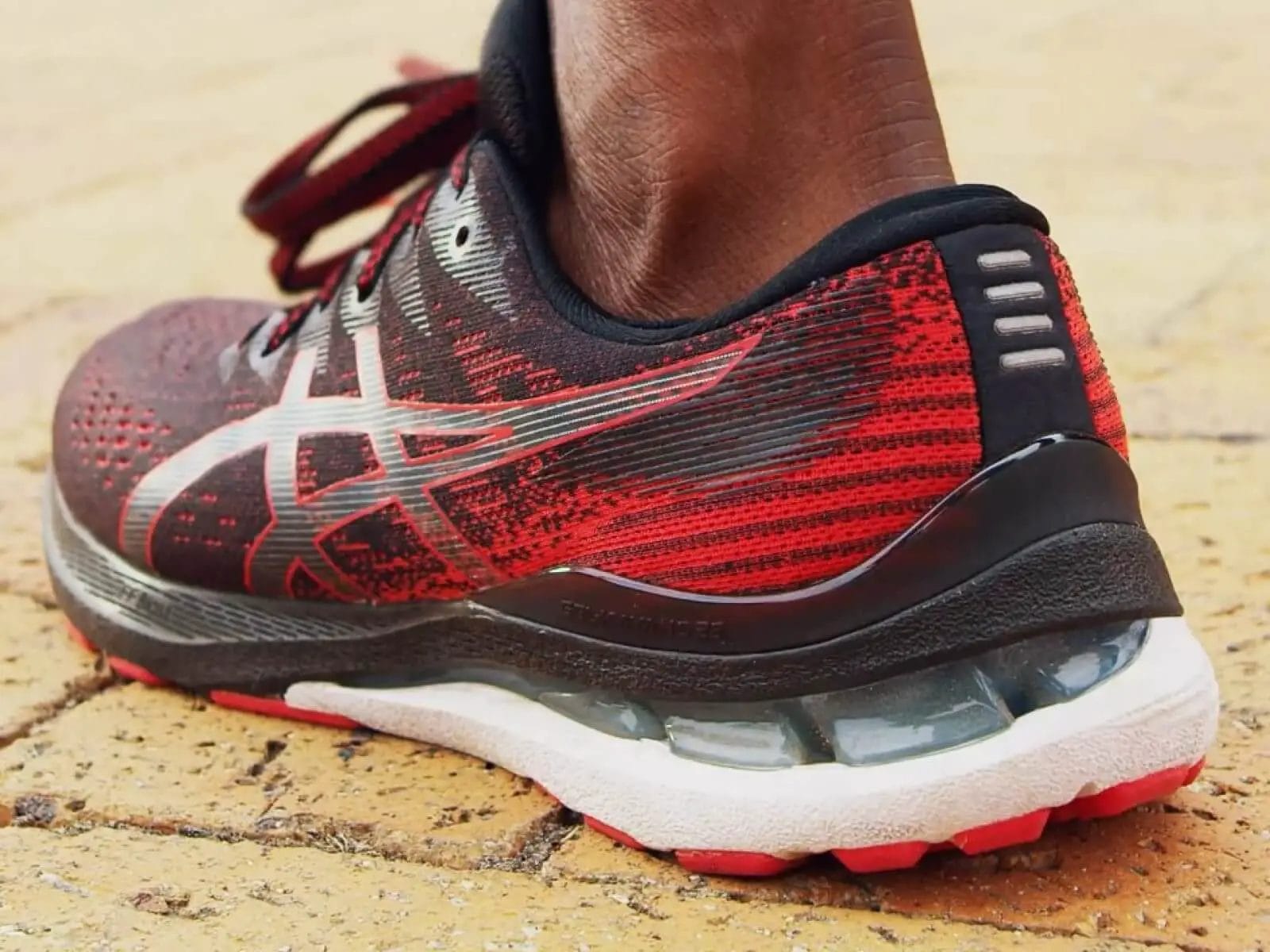 Details of the rear of the asics gel kayano 28 shoe while someone is running on pavement.