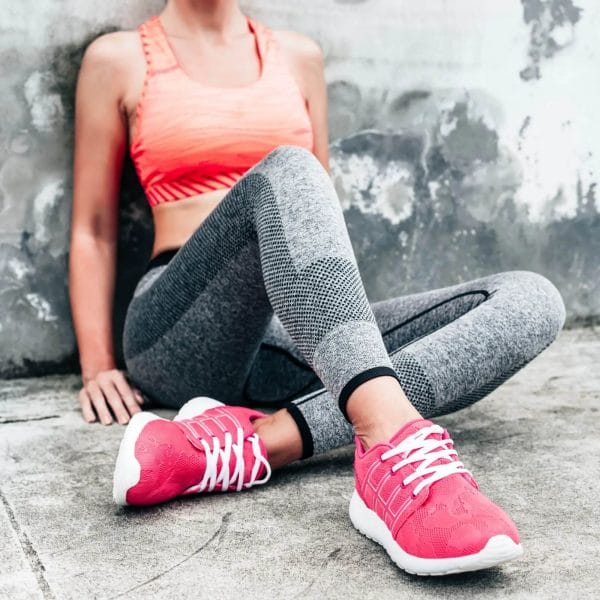 Woman with pink arch support running shoes sitting on sidewalk after workout.