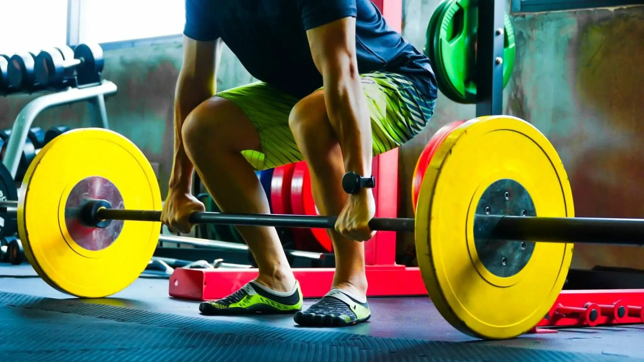 Powerlifter in minimalist squat shoes with yellow weights in gym.