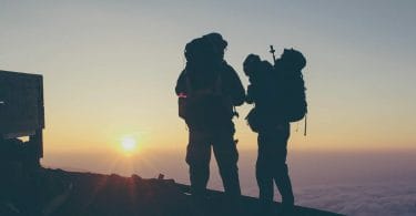 Two climbers on mountain summit at dawn with packs containing essential protective gear for hiking.