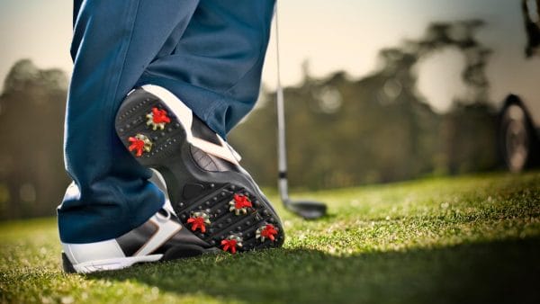 Person with red and white golf spikes leaning on iron.