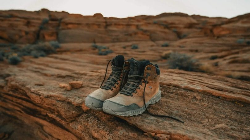 Pair of hiking boots with rubberized toe and reinforced gusseted tongue sitting on red rocks in the desert.