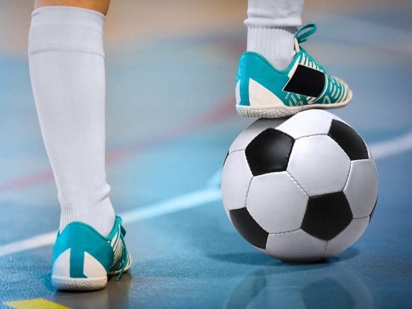 Flat soled indoor soccer shoes with person standing on ball.