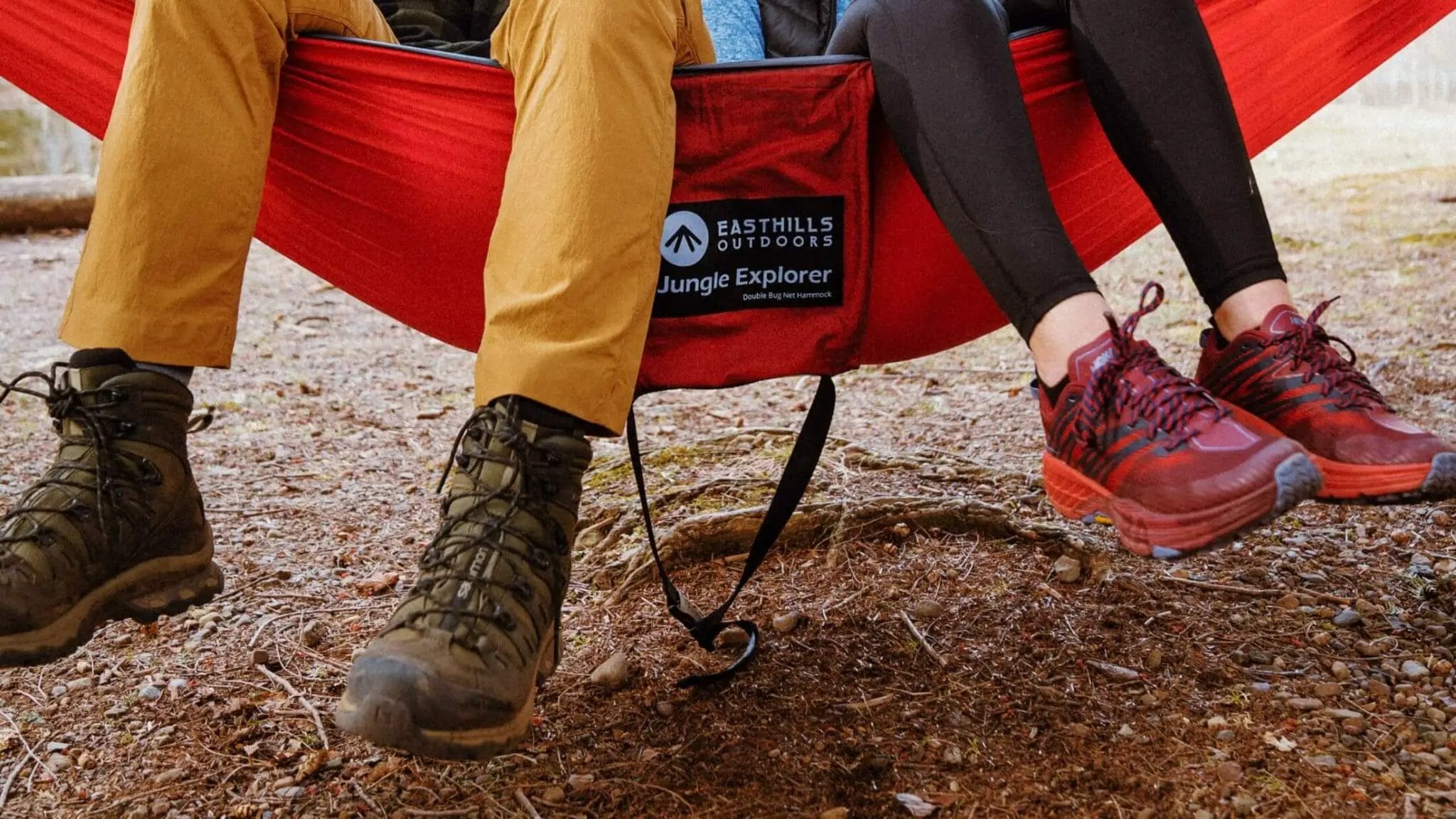 People sitting in a camping hammock with hiking shoes stretched over edge.