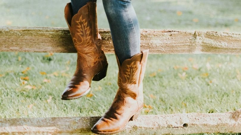 Woman wearing cowboy boots while sitting on wood fence in snake country.